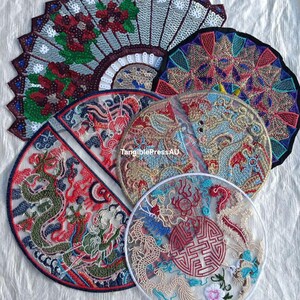 May include: A selection of embroidered patches with Asian-inspired designs. The patches feature dragons, floral patterns, and geometric shapes in red, blue, green, and gold. Some patches are fan-shaped, others are circular.