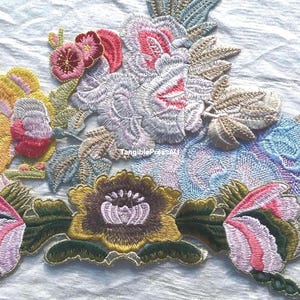 May include: An embroidered floral appliqué patch featuring a vibrant arrangement of flowers in shades of yellow, pink, blue, and dark green. The design includes intricate stitching details and the small text TangiblePressAU centred in the middle.