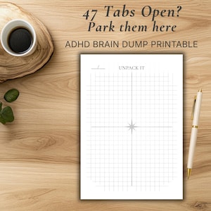 May include: A white printable notepad with a grid pattern and the text "Unpack It" and "ADHD Brain Dump Printable". A gold and white pen rests on the wooden surface next to the notepad. A cup of coffee and a small plant are also visible.