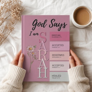 May include: A hardback book with a dusty rose cover featuring the text God Says I am SARAH in black and white lettering. The design includes a floral illustration and five colour-blocked rectangles with the words SPECIAL, ACCEPTED, REDEEMED, and HEALED.