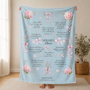 Peut inclure: Une couverture bleu clair ornée de bouquets d'hortensias roses liés par des rubans roses, avec du texte noir incluant le nom Mirabel Elena, la date du 22 octobre 2026 et divers versets bibliques comme Ésaïe 43:1, Jérémie 1:5 et Matthieu 3:17.