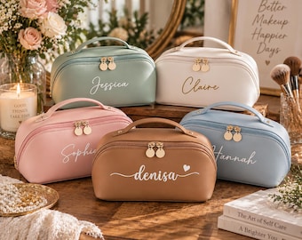 May include: Five dome-shaped cosmetic bags with top handles and dual gold-tone zipper pulls. The bags are in sage green, white, light pink, tan, and light blue, each featuring a custom name printed in white or gold script on the front panel.