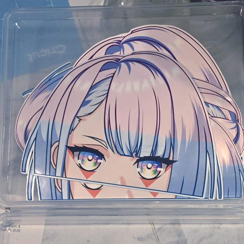 May include: A die-cut vinyl sticker featuring an anime-style character face with pale lavender hair, large expressive eyes with multicolored irises, and distinct red diamond-shaped markings beneath each eye, presented in a clear plastic case.