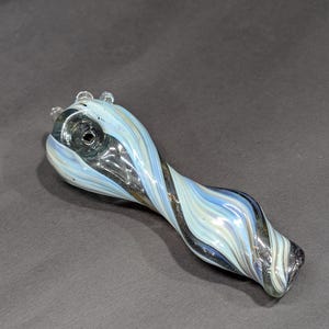 May include: A glass pipe with a swirling pattern in shades of blue, white, and black. The pipe features a rounded bowl and a curved stem. The stem's end is flattened and rounded. The pipe is made of clear glass.