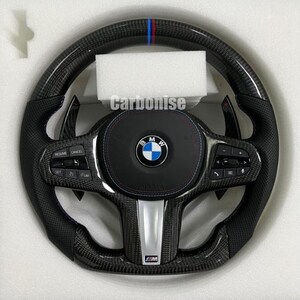 Op de afbeelding: Een carbon fiber stuurwiel met een zwarte lederen grip en blauwe, rode en witte accenten. Het stuurwiel heeft het BMW-logo, bedieningsknoppen en de tekst "Carbonise".