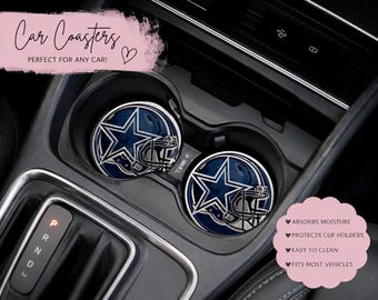 May include: Two circular car coasters featuring a dark blue and silver football helmet graphic with a prominent blue star logo. The coasters are positioned inside the cup holders of a vehicle center console, displaying a glossy finish.