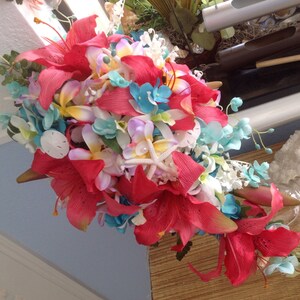 May include: A vibrant bouquet of red, pink, white, and blue flowers. The bouquet features lilies, orchids, and other tropical flowers. The flowers are arranged in a cascading style, with the stems extending out from the center.