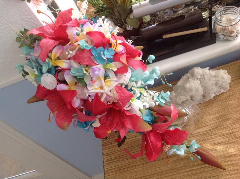 May include: A vibrant bouquet of red, pink, white, and blue flowers. The bouquet features lilies, orchids, and other tropical flowers. The flowers are arranged in a cascading style, with the stems extending out from the center.