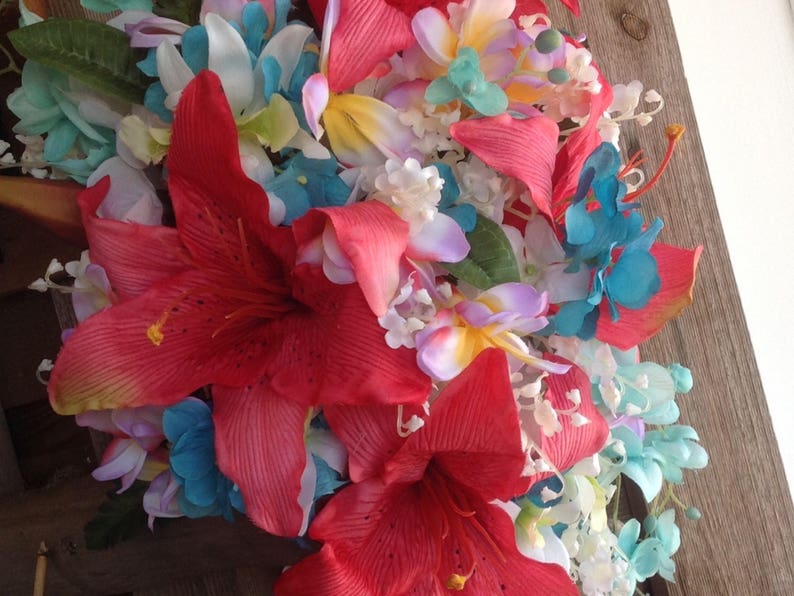 May include: A bouquet of artificial flowers with red, white, blue, and yellow flowers. The bouquet features a large red lily and smaller flowers in various shades of blue and white.