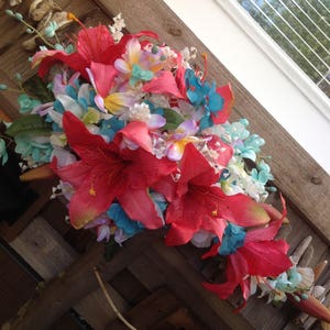 May include: A colorful bouquet of artificial flowers, featuring red, pink, white, and blue blooms. The flowers are arranged in a cascading style, with the red flowers being the most prominent.