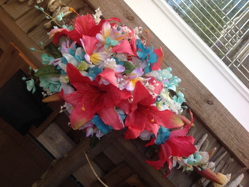 May include: A colorful bouquet of artificial flowers, featuring red, pink, white, and blue blooms. The flowers are arranged in a cascading style, with the red flowers being the most prominent.