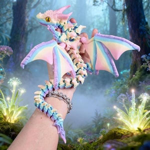 May include: A multi-coloured articulated dragon figurine featuring a pastel gradient of pink, blue, and yellow. The dragon has large wings, a segmented tail, and prominent yellow eyes with black pupils, designed with a flexible, jointed structure.