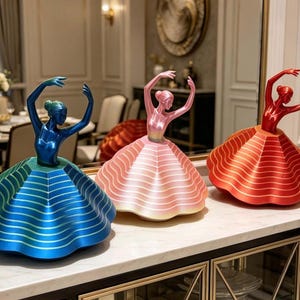 May include: Three decorative ballerina figurines. Each figurine has a different colour scheme: blue and green, pink and white, and red and orange. The ballerinas are posed with their arms raised, and their skirts are flared.