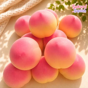 Può includere: Una collezione di giocattoli squishy rotondi a forma di pesca con una sfumatura di colore che passa da un rosa vivace sulla parte superiore a un giallo tenue alla base. Il testo Sakura Squish è visibile nell'angolo in alto a destra.
