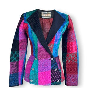May include: A double-breasted blazer featuring a vibrant patchwork design with quilted textures in shades of magenta, teal, blue, and black. The garment has a solid black lapel, long sleeves, and six silver-toned buttons. A Roots label is at the neck.