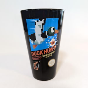May include: Black glass with the "Duck Hunt" logo. The design features a pixelated duck, the game's title, and the Nintendo logo. The glass has a slightly tapered shape.