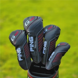 Puede incluir: Un juego de fundas para palos de golf negras con detalles rojos y blancos. Las fundas muestran la marca "PING" en blanco y el modelo "G410" en rojo. Las fundas están en una bolsa de golf sobre un fondo verde.