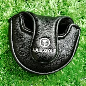 Puede incluir: Funda negra para putter de golf con el texto "L.A.B. GOLF" en blanco. La funda est&aacute; hecha de material texturizado y tiene forma redondeada con dos aberturas. La funda est&aacute; sobre una superficie verde. La marca "Yifu2Crafts" est&aacute; en la esquina superior izquierda.