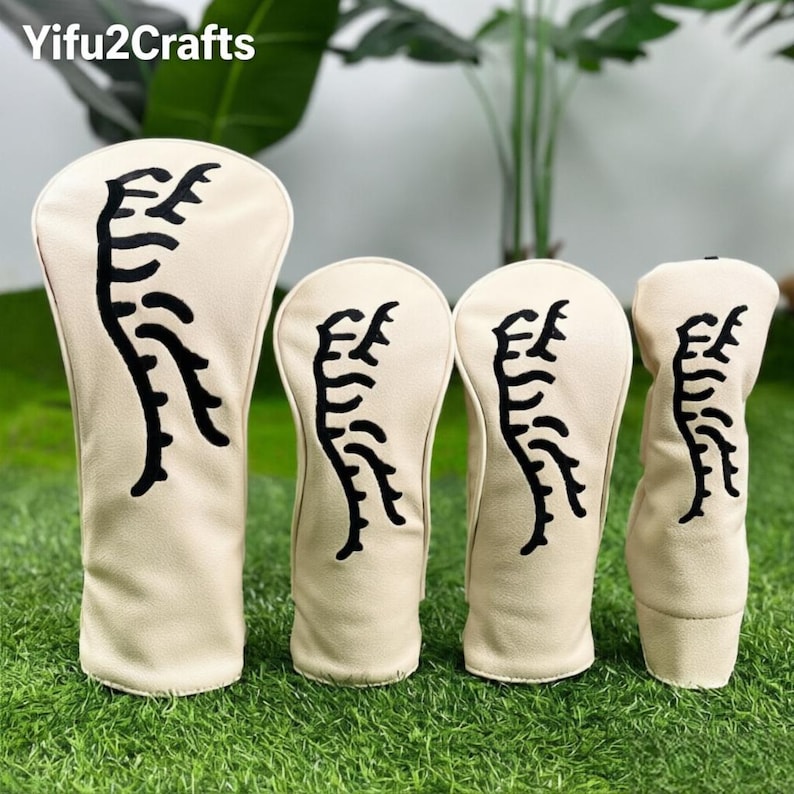 May include: A set of four golf club head covers. The covers are beige with a black abstract design. The covers are arranged on a bed of green grass. The brand name "Yifu2Crafts" is in the top left corner.