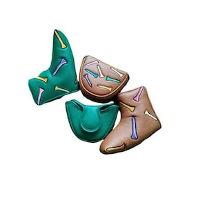 May include: Four golf club head covers in shades of green and brown. Each cover is decorated with a pattern of colorful golf tees. The covers are made of a leather-like material and are designed to protect golf clubs.