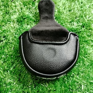 Puede incluir: Funda de putter de golf negra con una superficie texturizada y un mango negro suave. La funda est&aacute; colocada sobre un fondo de c&eacute;sped artificial verde. El texto "Yifu2Crafts" es visible en la parte superior.