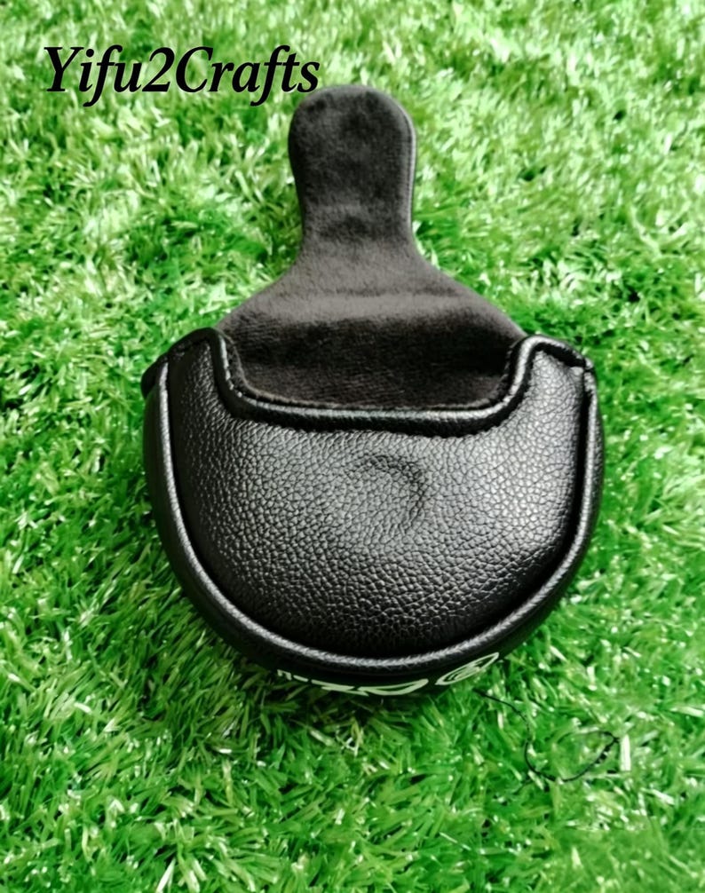 Puede incluir: Funda de putter de golf negra con una superficie texturizada y un mango negro suave. La funda est&aacute; colocada sobre un fondo de c&eacute;sped artificial verde. El texto "Yifu2Crafts" es visible en la parte superior.