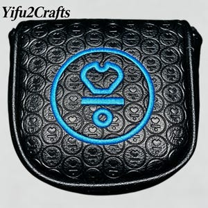 May include: Black golf club head cover with a blue embroidered design featuring a crown and circle. The cover has a textured pattern of circles and hearts. The text "Yifu2Crafts" is at the top.