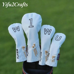 May include: A set of four white golf club head covers. The covers have black lettering and numbers, including the number 1, and the letters W and U. The covers have a textured design and small wooden golf tees attached. The brand name "MX Golf" is printed on the covers.