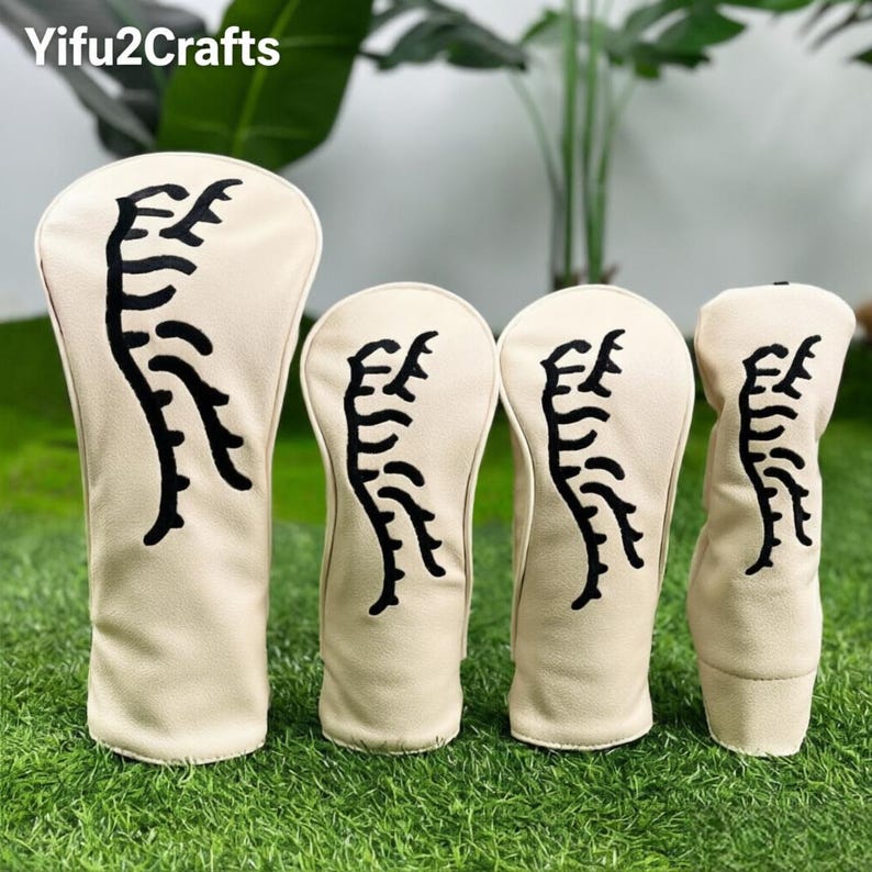 May include: A set of four golf club head covers. The covers are beige with a black abstract design. The covers are arranged on a bed of green grass. The brand name "Yifu2Crafts" is in the top left corner.