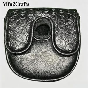 May include: Black leather golf putter cover with a textured surface and a flap closure. The cover features a circular pattern with heart-shaped designs. The interior is lined with a soft, dark material. The text "Yifu2Crafts" is at the top.