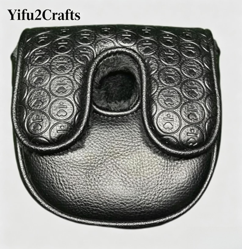 May include: Black leather golf putter cover with a textured surface and a flap closure. The cover features a circular pattern with heart-shaped designs. The interior is lined with a soft, dark material. The text "Yifu2Crafts" is at the top.