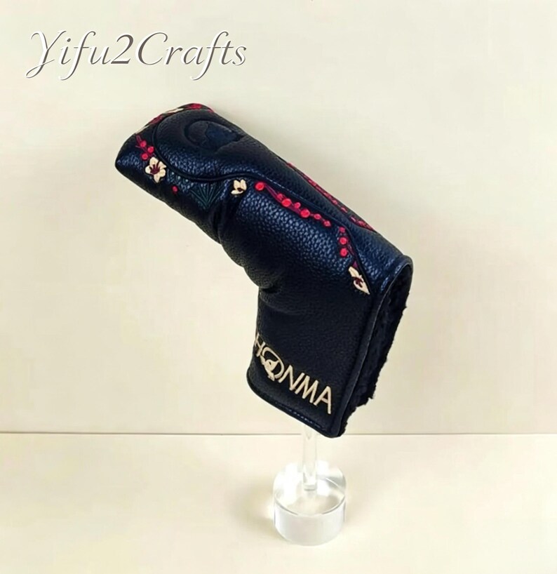 May include: Black golf club head cover with red and gold floral embroidery. The cover has the word "HONMA" in gold lettering. The text "Yifu2Crafts" is in the upper left corner.