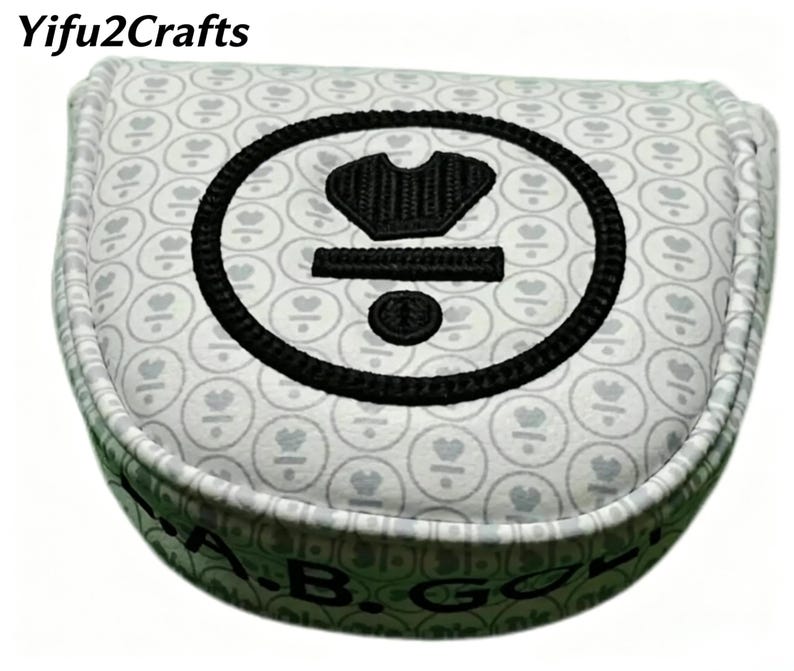 May include: A golf club head cover with a white background and a repeating pattern of gray hearts. The cover features a large black embroidered design and the text "A.B. GOLF" in green.