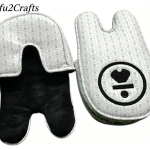 May include: Two oven mitts. The exterior is white with a repeating pattern of small gray floral designs. The interior is black. One mitt has a black circle with a crown design. The text "Yifu2Crafts" is at the top.