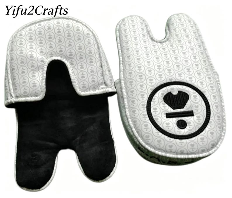 May include: Two oven mitts. The exterior is white with a repeating pattern of small gray floral designs. The interior is black. One mitt has a black circle with a crown design. The text "Yifu2Crafts" is at the top.