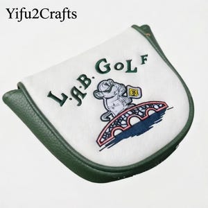 Könnte beinhalten: Weißer Golfschlägerkopfbezug mit grüner Umrandung. Der Bezug zeigt den Text "L.A.B. Golf" in Grün, zusammen mit einer gestickten Cartoonfigur auf einer Brücke. Der Markenname "Yifu2Crafts" befindet sich oben links.