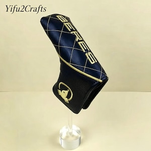 May include: A navy blue golf club head cover with gold stitching and the word "BERES" embroidered on the top. The cover has a diamond pattern and a gold emblem of a bird on the bottom. The brand name "Yifu2Crafts" is in the top left corner.