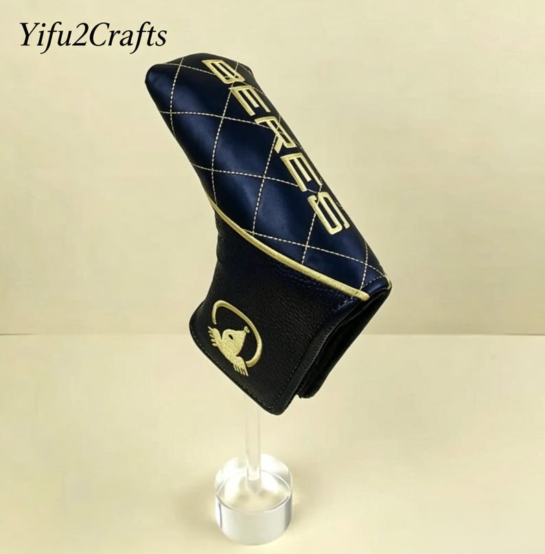 May include: A navy blue golf club head cover with gold stitching and the word "BERES" embroidered on the top. The cover has a diamond pattern and a gold emblem of a bird on the bottom. The brand name "Yifu2Crafts" is in the top left corner.