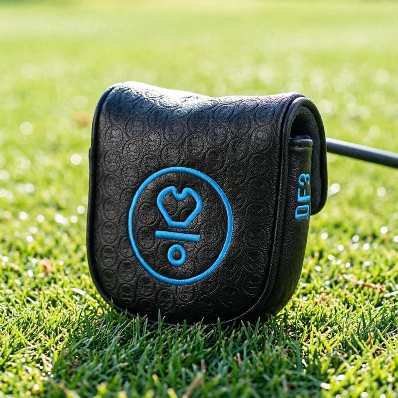 May include: Black golf putter cover with a blue circular logo and the text "DF3". The cover is on a green grassy surface. The logo features a heart-like shape and the number "3" inside a circle.