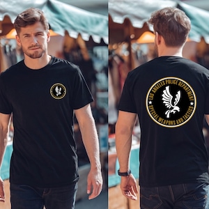 Può includere: Una t-shirt nera a maniche corte con un piccolo logo circolare sul petto sinistro e un grande logo circolare abbinato sul retro. Il logo mostra una grafica di un'aquila bianca circondata dal testo LOS ANGELES POLICE DEPARTMENT SPECIAL WEAPONS AND TACTICS.