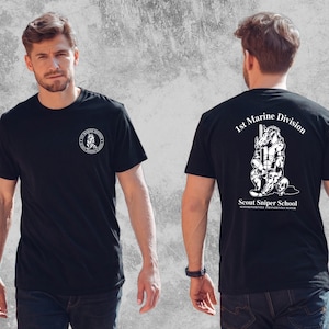 May include: A black t-shirt featuring a white graphic on the front left chest and a larger white graphic on the back. The back design depicts a hog mascot with a rifle, the text 1st Marine Division, Scout Sniper School, and Suffer Patiently.