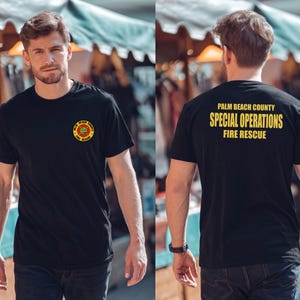 May include: A black short-sleeved t-shirt featuring a circular Palm Beach County Fire Rescue logo on the left chest. The back of the shirt displays the yellow text Palm Beach County Special Operations Fire Rescue in a bold, sans-serif font.