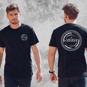 Könnte beinhalten: Ein schwarzes kurzärmeliges T-Shirt mit einem kleinen kreisförmigen weißen Logo auf der linken Brust und einer großen kreisförmigen weißen Grafik auf der Rückseite. Die Grafik auf dem Rücken zeigt den Text Triple Canopy A Constellis Company High Threat Protection Secure Success.