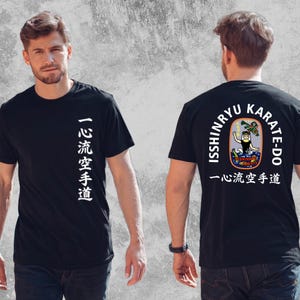 以下が含まれることがあります： 前面に白い日本語の漢字がプリントされた黒いTシャツ。背面には「ISSHINRYU KARATE-DO」の文字が円形に配置され、その中央に人物、龍、虎が描かれたカラフルなグラフィックと、その下に日本語の文字がデザインされています。