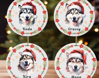 May include: Four round Christmas ornaments featuring watercolor portraits of husky dogs wearing Santa hats. Each ornament has a name: Koda, Gracey, Kira, and Maya. The ornaments are decorated with red poinsettias and gold accents.