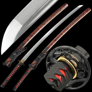 Op de afbeelding: Een Japanse katana-zwaard met een zilveren lemmet en een rood-zwarte handgreep. De handgreep heeft een ruitpatroon met rode accenten. De schede van het zwaard is zichtbaar op de achtergrond.