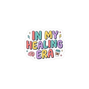May include: A die-cut sticker featuring the text IN MY HEALING ERA in colorful, rounded bubble letters. The design includes a small pink brain with a bandage, a coffee cup, and several small lightning bolt and star icons in pastel colors.