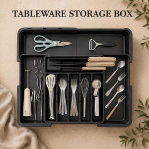 K&ouml;nnte beinhalten: Schwarze Besteck-Aufbewahrungsbox mit verschiedenen K&uuml;chenutensilien, darunter eine Schere, ein Sparsch&auml;ler, Schneebesen, L&ouml;ffel, Gabeln und ein Eisportionierer. Die Box ist offen und zeigt mehrere F&auml;cher zur organisierten Aufbewahrung. Der Text "TABLEWARE STORAGE BOX" steht oben.