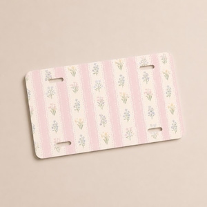 Op de afbeelding: Rechthoekige nummerplaat met een bloemenpatroon. Het ontwerp bevat verticale roze strepen met een kantachtige rand, afgewisseld met kleine bloemenillustraties in pastelkleuren. De plaat heeft vier montagegaten.