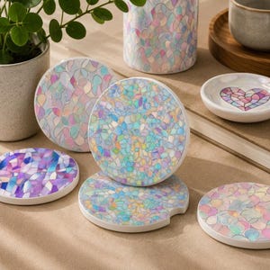 May include: A collection of circular coasters and a small dish featuring a mosaic-style iridescent pattern with pastel shades of pink, blue, and purple. The coasters have a smooth, glossy finish and a notched edge, displaying a shimmering, reflective surface.